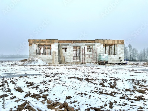 Front view of a house building in progress - concrete brick walls with some wooden elements to support the concrete. Construction and mason work during heavy winter and snow in Poland.