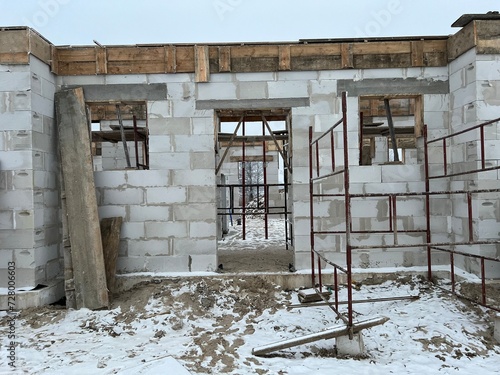 Font view of a house building in progress - fresh cement brick walls with holes for windows and door. Mason's work of home construction.