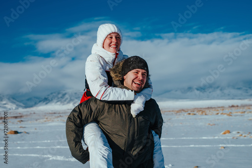 Happy young couple of tourists having fun in the snowy mountains in winter, man carries woman on his back