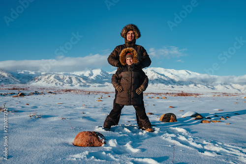 Happy father and child in winter clothes with hoods on mountains background