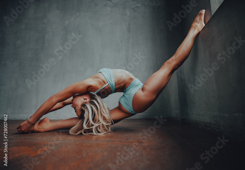 Young blond woman gymnast stretching on wall background