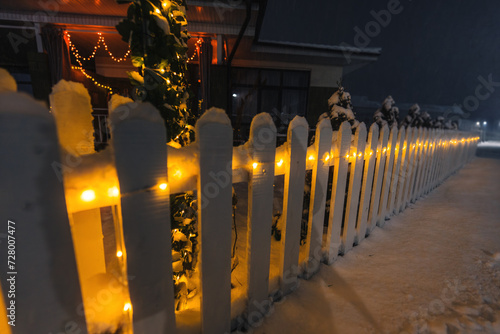 Fence of country cottage with garland on winter night