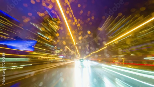 Back car window view of long exposure time laps of the highway in the city. City at night timelapse. Driving a car, the city at night. Camera at the vehicle back trunk glass. Rainy night soft glowing.