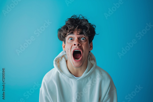 Young guy on a blue background screaming, frightened facial expression, panic scream