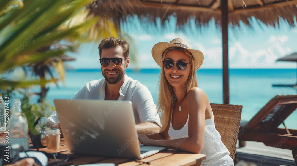 Smiling couple enjoying beach vacation and working , workcation on laptop, relaxation in work and life with embracing happiness by the sea, Travel and work concept.