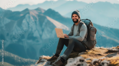 A man hikes and sitting on top of a mountain and working or workcation on laptop with enjoys a break look at the top of the mountain, adventure travel and work concept.
 photo