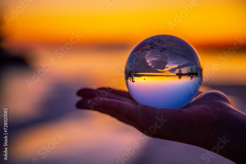Hand holding globe with reflection of the beach during a sunrise