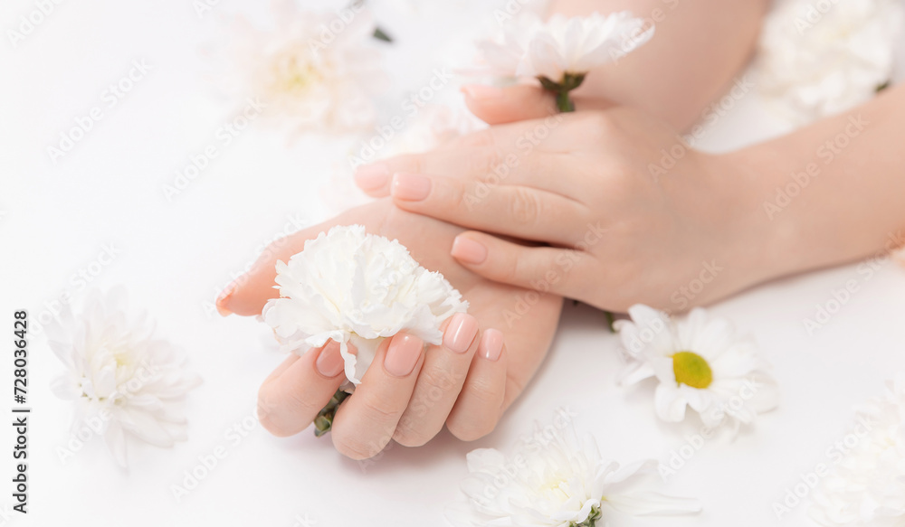 Concept cosmetic cream and beauty health care. Stylish trendy nail young woman hands pink manicure on white background with flowers, top view