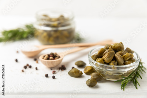 Capers in a bowl on a wooden kitchen table. Capers with sea salt and rosemary. Pickled capers.Mediterranean cuisine ingredient. Organic spices and seasonings. Copy space. © Avocado_studio