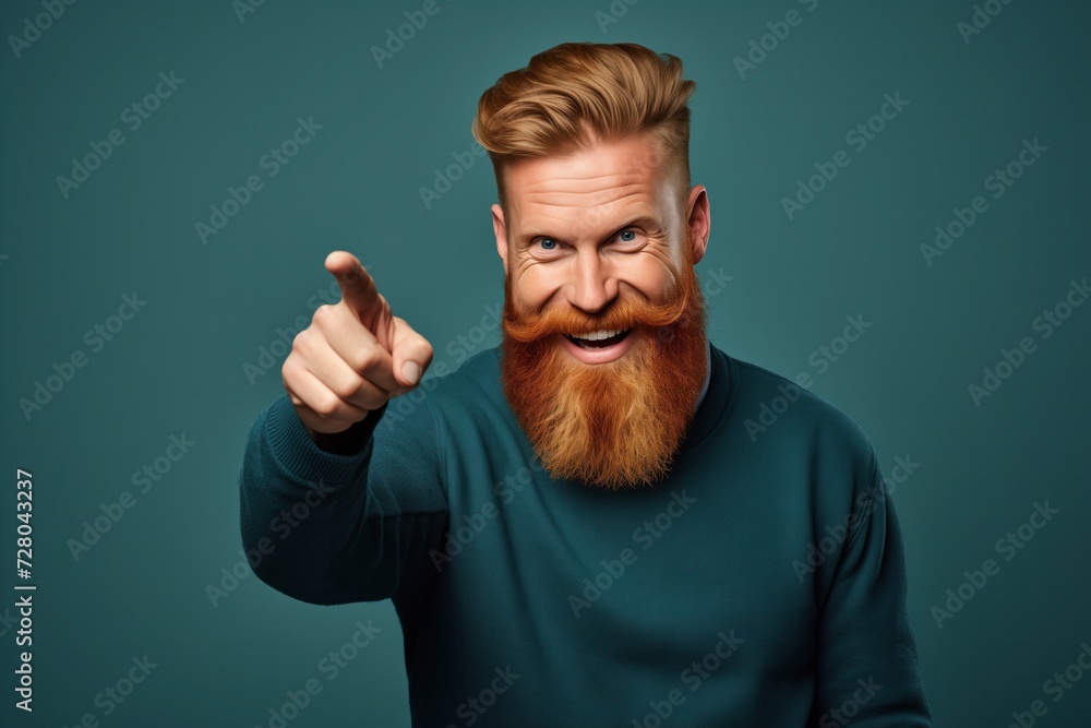 © Oleg Kozlovskiy - A man with a striking red beard and styled hair winks and points towards the camera, displaying a playful and engaging demeanor against a teal background