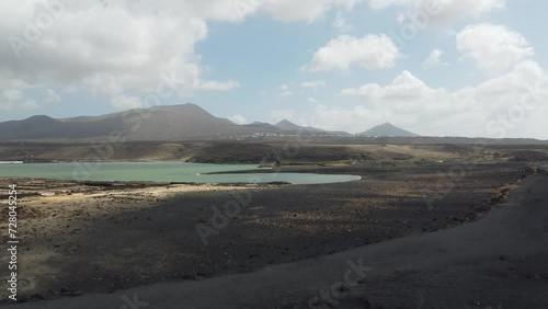 drone shot of a descent from above on black beach with clouds passing and ocean and mountains. 
lanzarote, spain