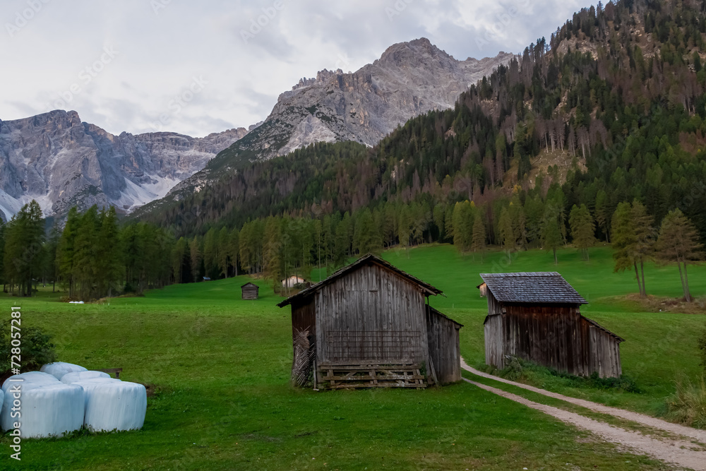Scenic hiking trail along wooden huts on idyllic alpine meadow with awe view of majestic mountain peaks of Sexten Dolomites, South Tyrol, Italy, Europe. Hiking in panoramic Fischleintal, Italian Alps