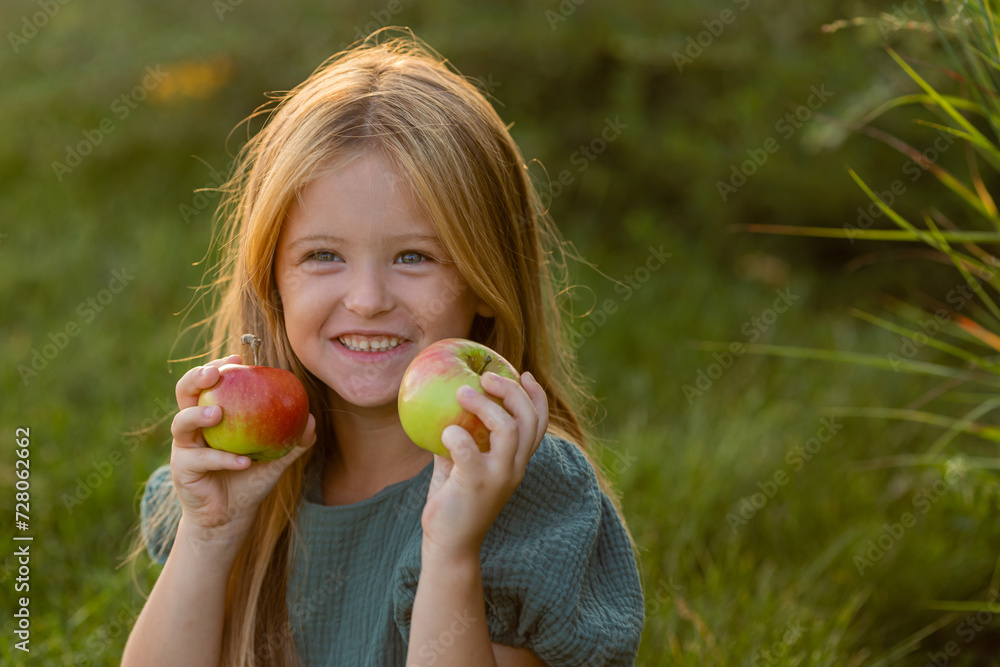 beautiful little girl with long blonde hair sits on the lawn in summer eating green apples beautiful little girl with long blonde hair sits on the lawn in summer eating green apples