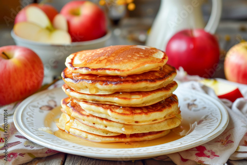 Stack of homemade apple pancakes on a white plate with fresh apples in the background