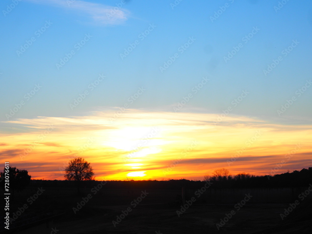 Sunset in the countryside, red, orange, and blue with trees.