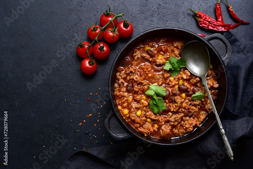 Chili con carne - traditional mexican minced meat and vegetables stew in tomato sauce in a cast iron pan . Top view with copy space.