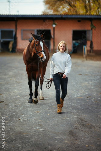 Young woman in civilian clothes leads her horse across the stables. © RD-Fotografie