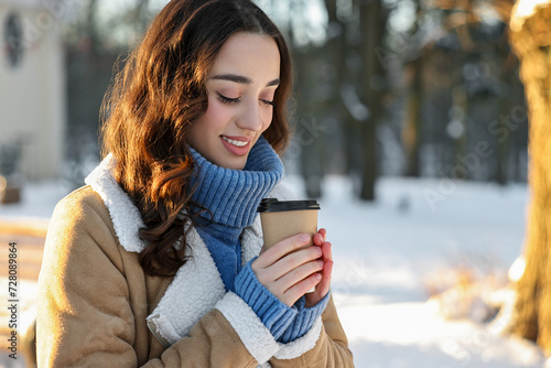 Portrait of smiling woman with paper cup of coffee in snowy park. Space for text