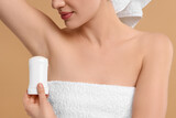 Woman applying deodorant on beige background, closeup