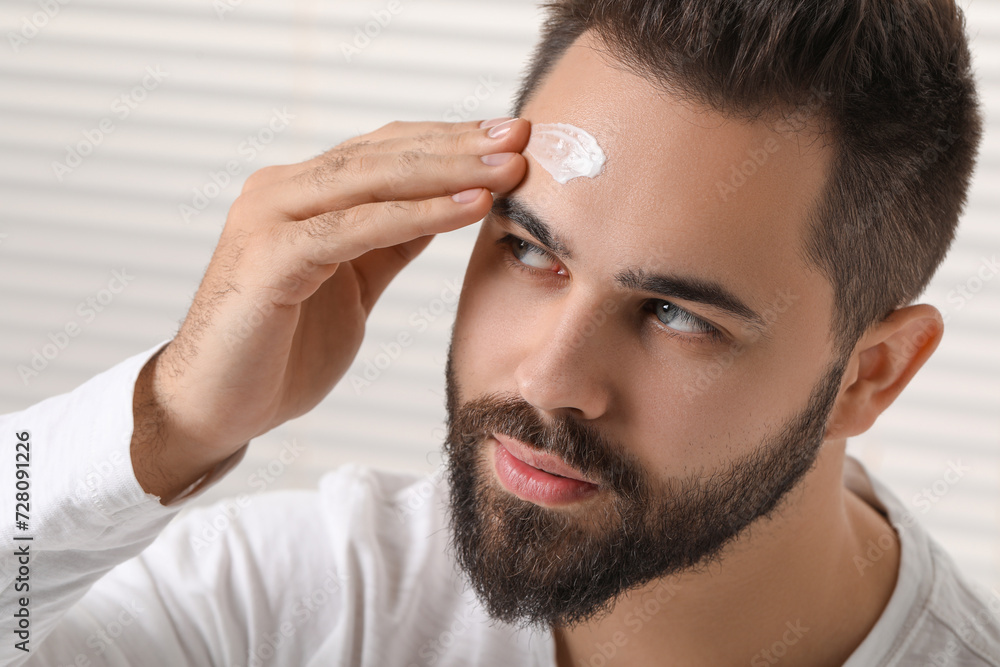 Obraz premium Man with dry skin applying cream onto his forehead indoors