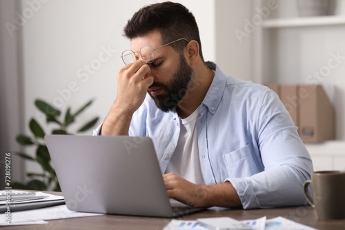 Man with glasses suffering from headache at workplace in office