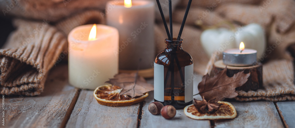 Concept of cozy fall home atmosphere, aromatherapy. Perfume, apartment aroma diffuser with autumn scent of pumpkin spicy sweet pie, cinnamon, anise. Room decor: pumpkins, dry orange, wool plaid banner