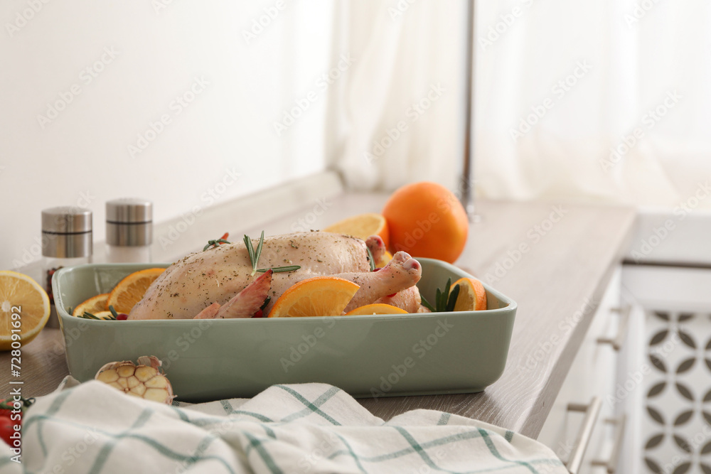 Chicken with orange slices in baking pan on wooden countertop
