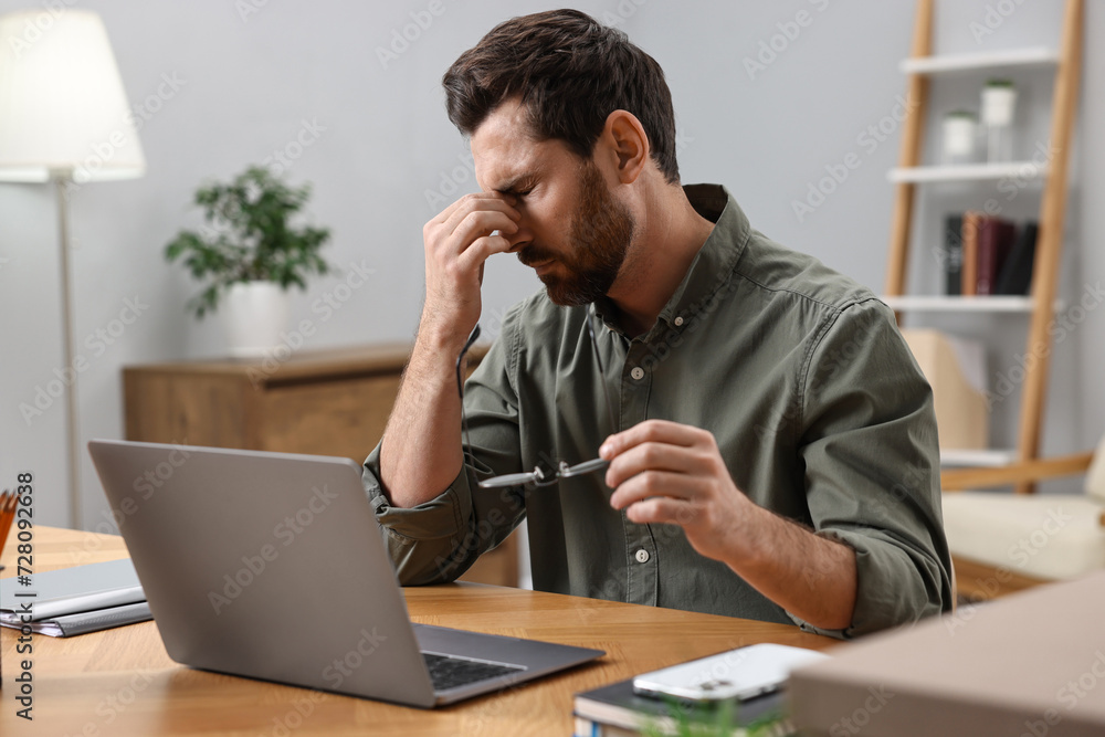 Naklejka premium Tired man suffering from headache at workplace