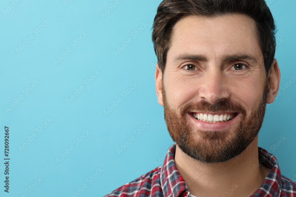 Fototapeta premium Portrait of smiling man with healthy clean teeth on light blue background, closeup. Space for text