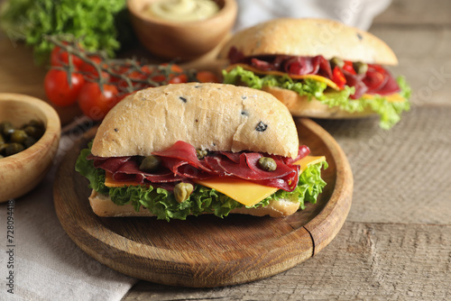 Delicious sandwiches with bresaola, cheese and lettuce served on wooden table, closeup