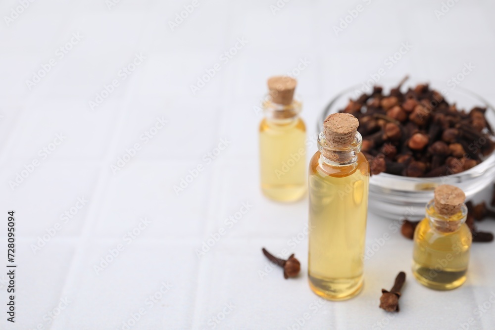 Clove oil in bottles and bowl with dried buds on white tiled table, space for text Clove oil in bottles and bowl with dried buds on white tiled table, space for text
