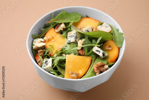 Tasty salad with persimmon, blue cheese and walnuts served on light brown background