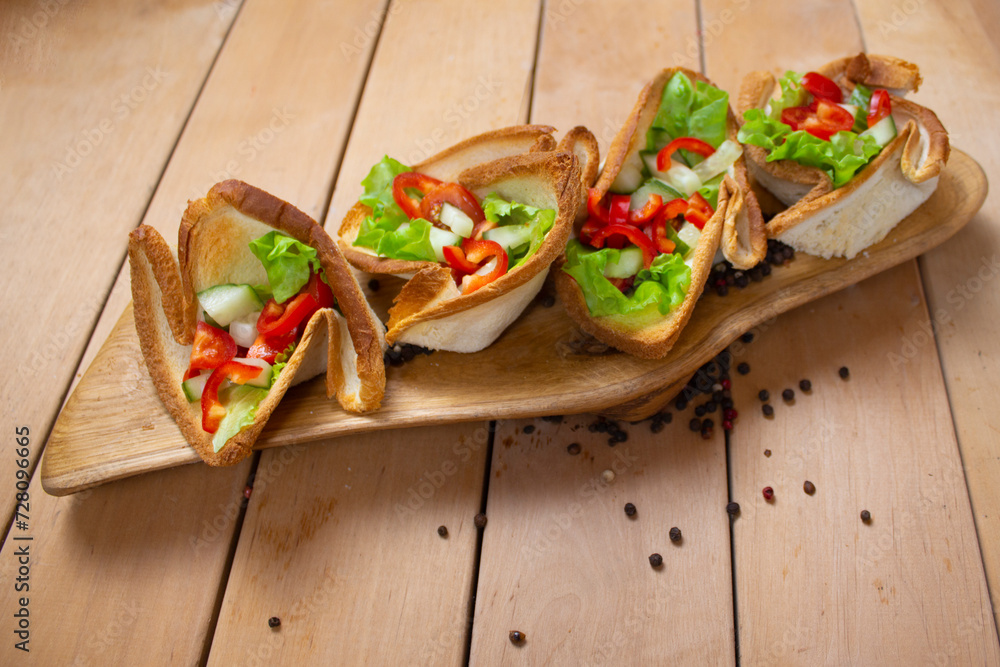 Salad with in tartlets on a board on a wooden table. Tartlets are made from toasted bread. Concept: edible food utensils.