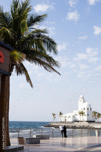 Young muslim couple enjoying a sunny hot day in Jeddah watching the Red Sea and a white mosque on the background