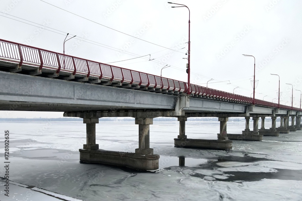 Road bridge on winter river. Large concrete bridge with red railings and lamp posts, river is covered with ice.