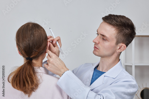 Otoplasty markup for surgical reshaping of the pinna, or outer ear for correcting an irregularity and improving appearance. Surgeon doctor marking girl ear before otoplasty cosmetic surgery photo