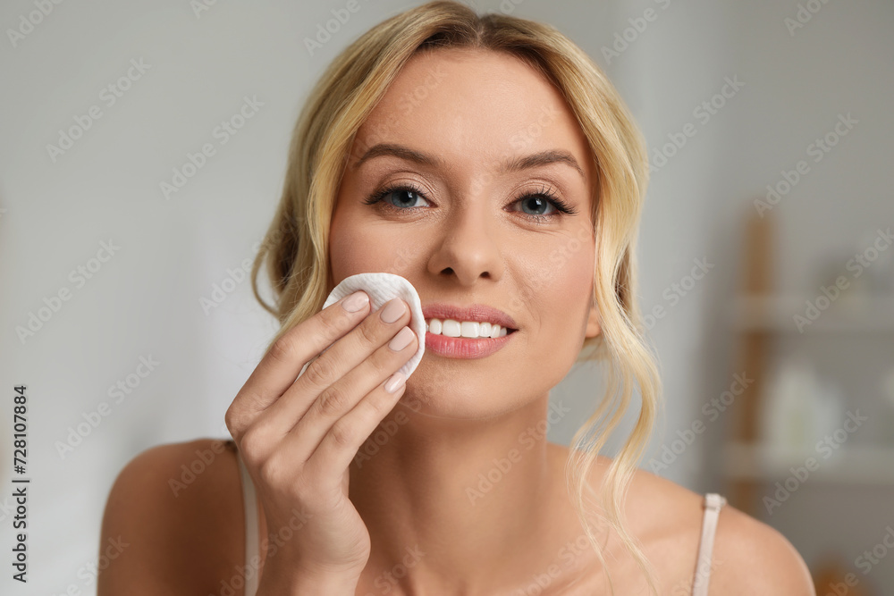 Smiling woman removing makeup with cotton pad indoors, closeup Smiling woman removing makeup with cotton pad indoors, closeup