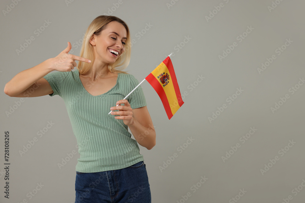 Happy woman pointing at flag of Spain on grey background, space for text Happy woman pointing at flag of Spain on grey background, space for text