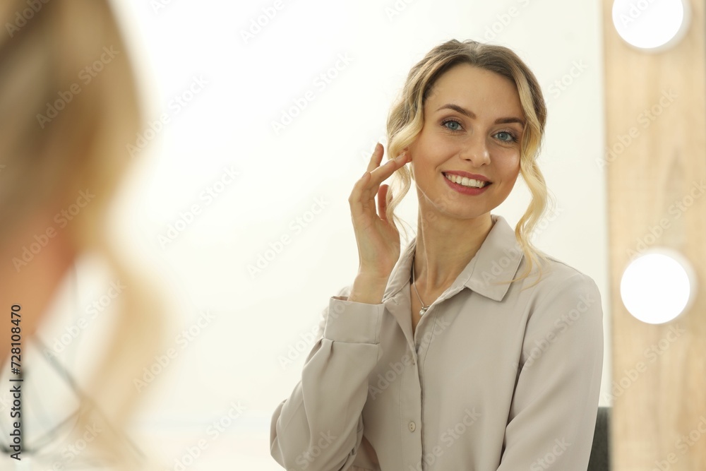 Smiling woman with beautiful hair style looking at mirror indoors Smiling woman with beautiful hair style looking at mirror indoors