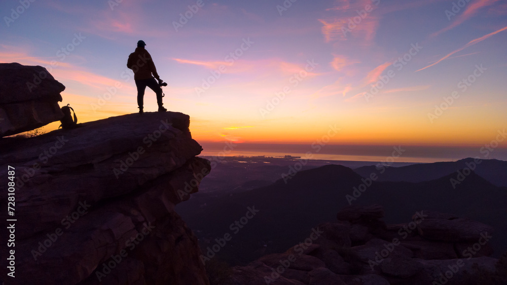 Silueta de joven aventurero en lo alto de la montaña al amanecer. 