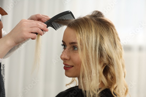 Hair styling. Professional hairdresser combing woman's hair in salon, closeup