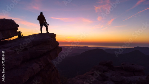 Silueta de joven aventurero en lo alto de la montaña al amanecer. 