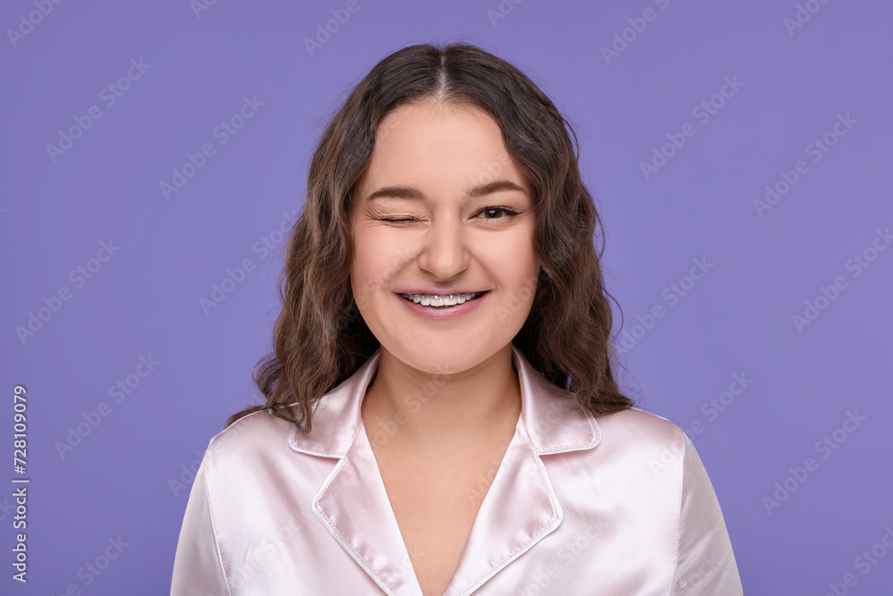 Smiling woman with braces winking on violet background Smiling woman with braces winking on violet background