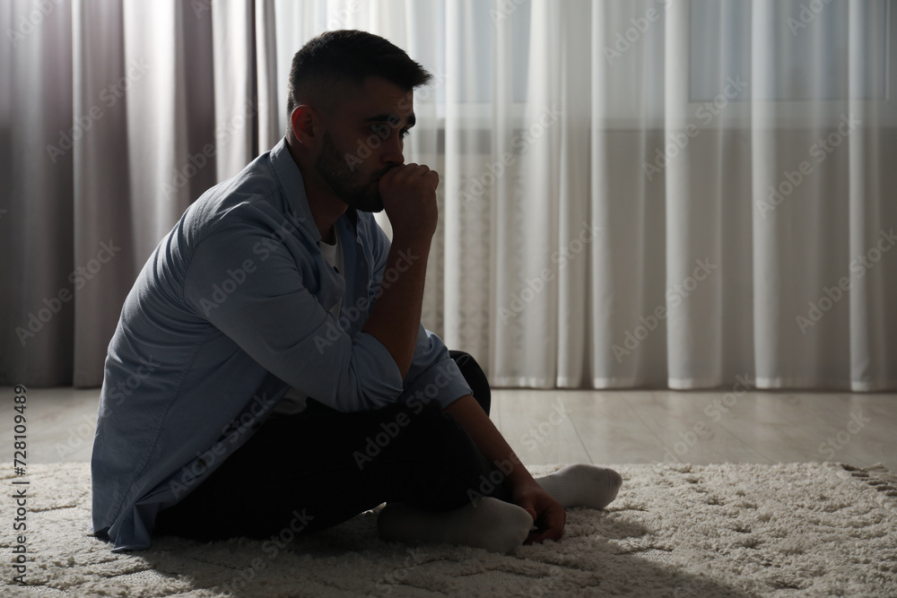 Sad man sitting on floor near window. Space for text Sad man sitting on floor near window. Space for text
