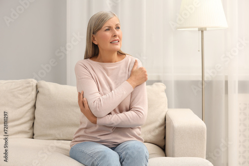 Mature woman suffering from pain in arm on sofa at home. Rheumatism symptom