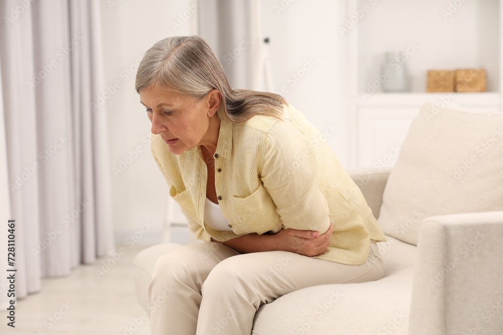 Menopause. Woman suffering from abdominal pain on sofa at home Menopause. Woman suffering from abdominal pain on sofa at home