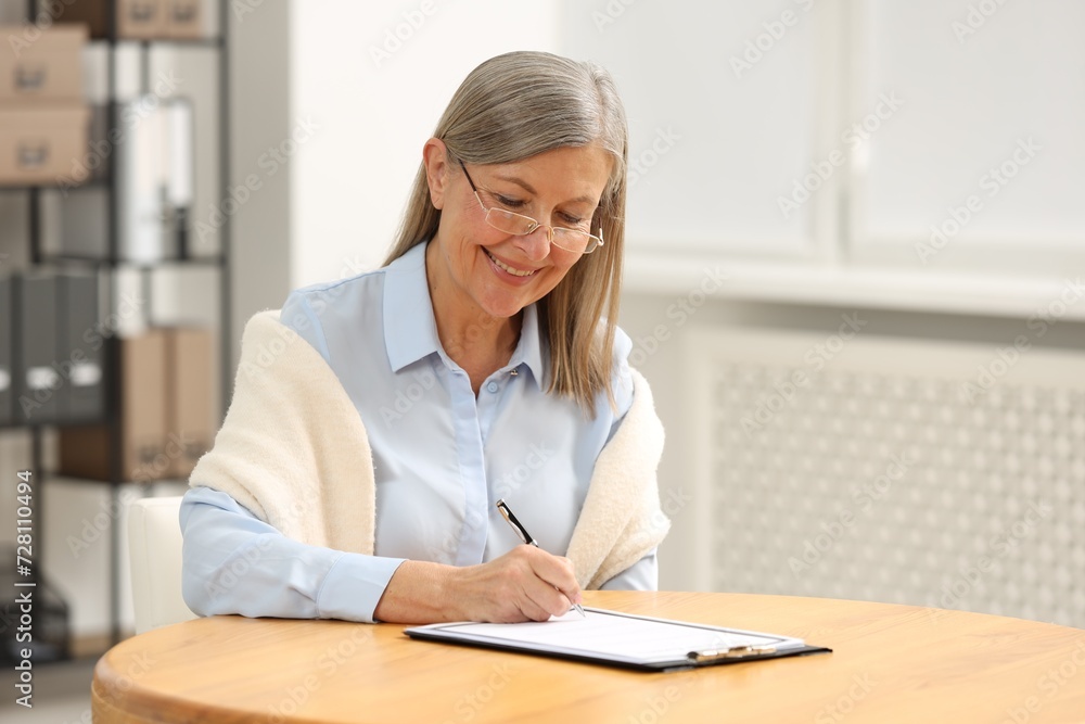 Smiling senior woman signing Last Will and Testament at table indoors Smiling senior woman signing Last Will and Testament at table indoors