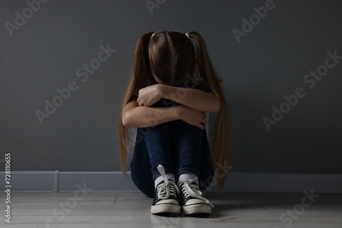 Sad girl sitting on floor near dark grey wall indoors