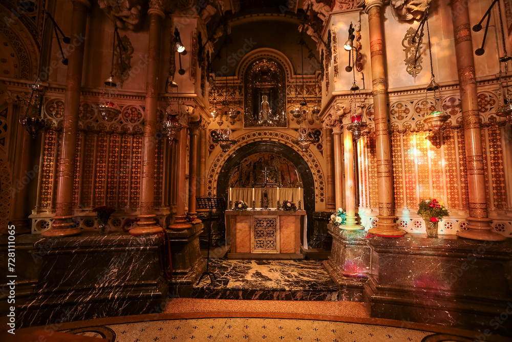 In a Barcelona chapel, an arch encircles the altar and a sacred icon, set against gold, red, and cream designs. The walls, pillars, and marble boast detailed patterns, while lamps cast a gentle light.
