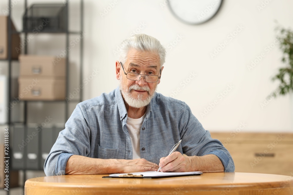 Senior man signing Last Will and Testament at table indoors Senior man signing Last Will and Testament at table indoors